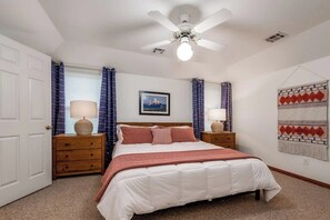 A bedroom with a bed, two bedside tables, a ceiling fan, and a wall-mounted artwork. - 4BR with private pool, patio & firepit (Bentonville)