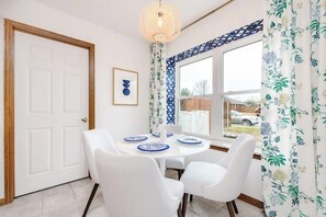 A dining area with a white table and chairs, a hanging light fixture, and a window with patterned curtains. - 4BR with private pool, patio & firepit (Bentonville)