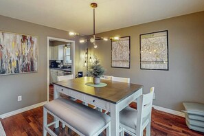 Un espace repas comprenant une table en bois, des chaises blanches, un banc et un luminaire suspendu.