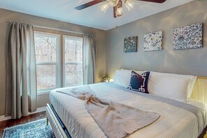 Une chambre à coucher avec un lit, des rideaux, un ventilateur de plafond et des œuvres d’art murales.