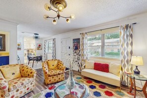 A living room with a sofa, armchair, and a coffee table with a vase. There is a dining area in the background. - 2BR Modern condo with shared hot tub & pool access (Hot Springs)