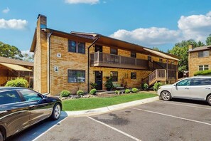 A two-story building with a brick facade, a balcony on the second floor, and a parking lot with two cars. - 2BR Modern condo with shared hot tub & pool access (Hot Springs)