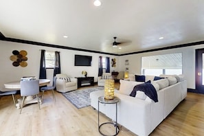A modern living room with a white sofa, a dining table with chairs, a small side table with a lamp, and a ceiling fan. - Sophisticated Waterfront Home with Private Dock (Hot Springs)
