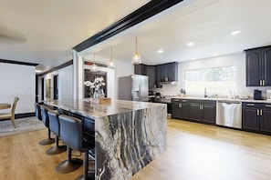 A modern kitchen with a marble island, bar stools, dark cabinets, and pendant lighting. - Sophisticated Waterfront Home with Private Dock (Hot Springs)