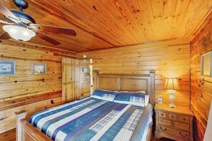 A wooden cabin bedroom with a bed, nightstand, dresser, ceiling fan, and framed pictures on the walls. - 3BR Apartment - Riverfront - River Access - WIFI (Hot Springs)