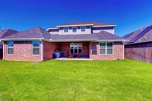 Casa de dos plantas con fachada de ladrillo, un porche cubierto con mobiliario exterior y un patio trasero cercado.