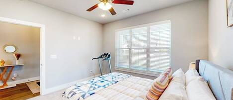 A bedroom with a bed, a ceiling fan, a treadmill, and a window with blinds.