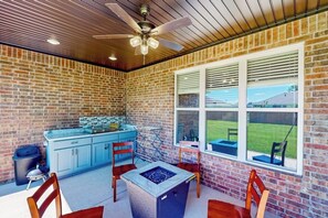 A covered patio area with a brick wall, a ceiling fan, a kitchen counter, and a dining table with chairs. - 4BR home with foosball & children's items, dogs ok (Bentonville)