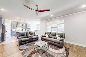 A spacious living room with a ceiling fan, two leather sofas, a coffee table, and a kitchen in the background. - 4BR home with foosball & children's items, dogs ok (Bentonville)