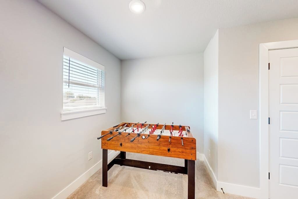 A room with a foosball table, a window with blinds, and a white door.