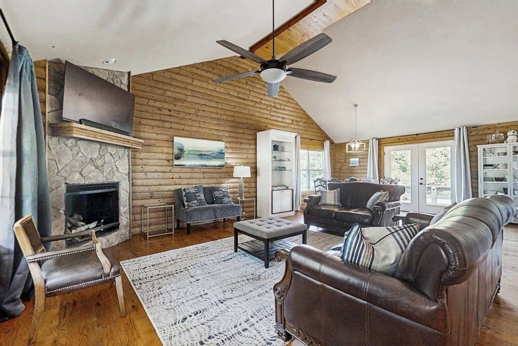 L’intérieur d’une cabane en rondins, avec une cheminée, un canapé en cuir et un ventilateur de plafond.
