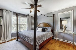 A bedroom with a four-poster bed, a ceiling fan, a bedside table with a lamp, and a large window with curtains. - 5BR Spacious family retreat with pool, BBQ grill (Rogers)