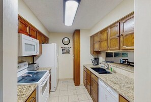 Eine kleine Küche mit Holzausstattung, einer Mikrowelle, einem Kühlschrank, einem Herd, einer Spüle und einer Kaffeemaschine.