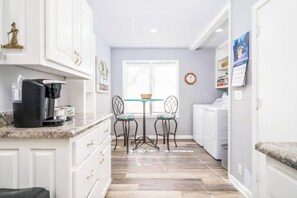 Una cocina compacta con armarios blancos, cafetera, fregadero y ventana con vistas.