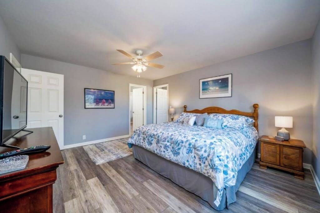 A bedroom with a bed, a ceiling fan, a nightstand, a lamp, a dresser, and a television.