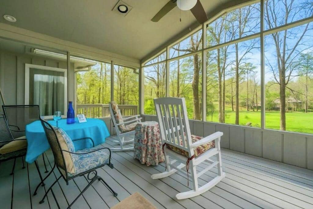 A covered outdoor area with a table and chairs, large windows, and a view of a green landscape.