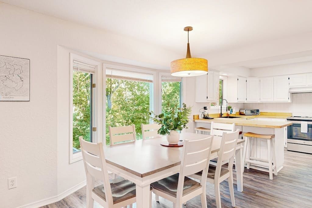 A bright kitchen with white cabinets, a wooden dining table, and a hanging light fixture.