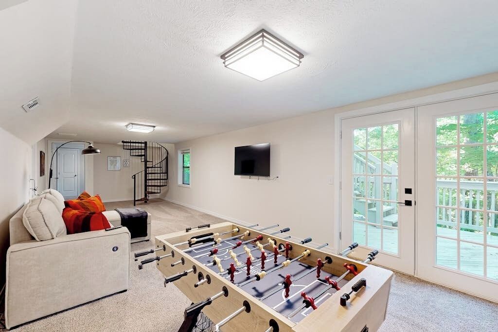 A room with a foosball table, a sofa, a television mounted on the wall, and a staircase leading to another level.