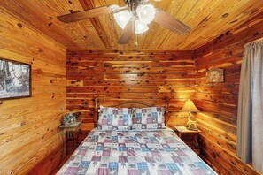 A wooden cabin bedroom with a bed, a ceiling fan, a nightstand, a lamp, and a framed picture on the wall. - 1BR Condo - Riverfront - Fishing - Full Kitchen (Hot Springs)