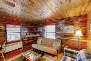 A log cabin interior with a sofa, a plaid chair, a table with magazines, and a floor lamp. - 1BR Condo - Riverfront - Fishing - Full Kitchen (Hot Springs)