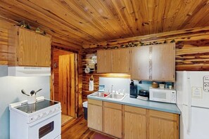 Cocina compacta con gabinetes de madera, estufa, microondas y refrigerador.