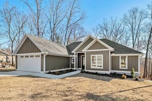 A two-story residential building with a garage, a covered entryway, and a landscaped front yard. - The Dutchman | 4BR, Deck, Firepit & Fireplace (Bella Vista)