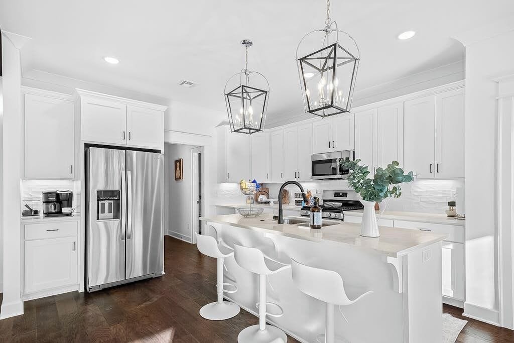A modern kitchen with white cabinetry, stainless steel appliances, and a central island with bar stools.