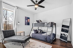 Une pièce comprenant un lit superposé, un canapé, une petite table, un ventilateur de plafond et un grand miroir.