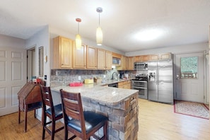 A kitchen with granite countertops, wooden cabinets, a central island with seating, stainless steel appliances, and pendant lighting. - 4BR Waterfront - Screen-in Deck (Eureka Springs)