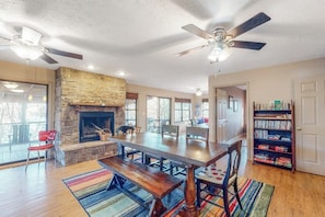 A spacious living area with a fireplace, a large wooden dining table, and a bookshelf. - 4BR Waterfront - Screen-in Deck (Eureka Springs)
