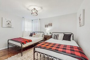 A bedroom with two single beds, a window with curtains, a wall-mounted light fixture, and a framed picture. - Large 3BR - Balcony - Firepit - Garage Parking (Bentonville)