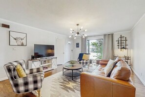 A modern living room with a television, a sofa, a chair, and a coffee table. - Large 3BR - Balcony - Firepit - Garage Parking (Bentonville)