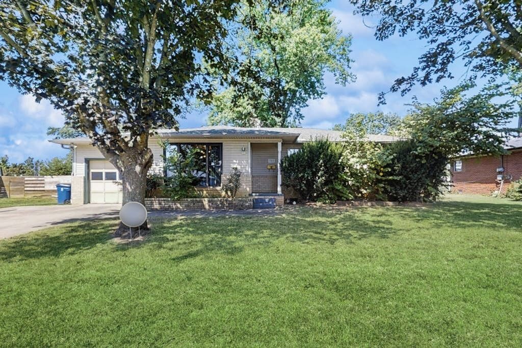 Ein Bungalow mit Garage, Rasen und einem Baum im Vordergrund.
