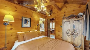 Ein Zimmer in einer Holzhütte mit einem Bett, einem Deckenventilator und einem Kleiderschrank.