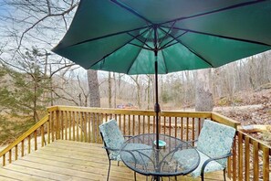 A wooden deck with a table and chairs under a green umbrella.