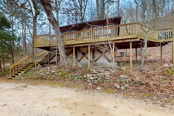 A wooden cabin with a balcony, a staircase, and a stone wall foundation.
