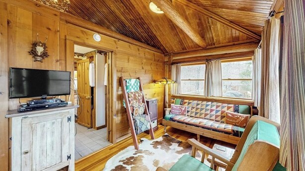 Ein gemütliches Blockhaus-Interieur mit Fernseher, einer Couch und einer Holzbalkendecke.
