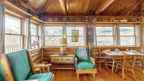 Ein Blockhaus-Interieur mit Holzwänden, einem Essbereich mit Tisch und Stühlen sowie einer Sitzecke mit Sofa und Sesseln.
