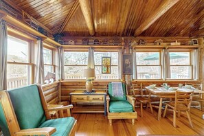 A log cabin interior with wooden walls, a dining area with a table and chairs, and a seating area with a sofa and armchairs.