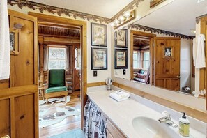 A bathroom with a large mirror, wooden walls, a sink, and a green chair.