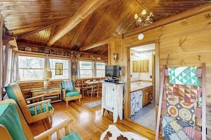 A wooden cabin interior with a dining area, seating, and a television.