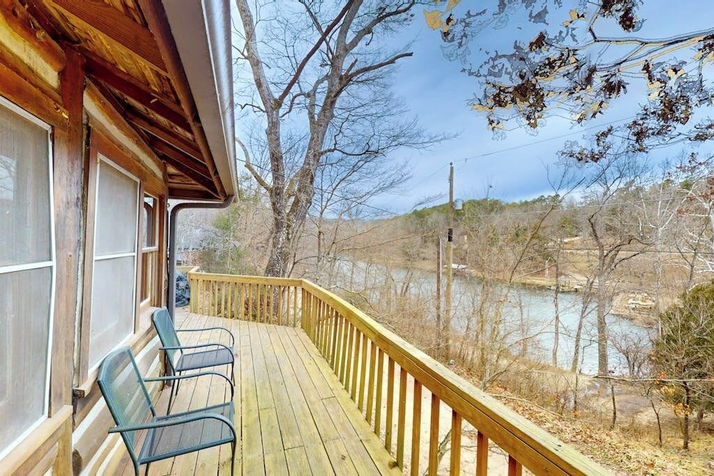 A wooden deck with a railing overlooking a body of water, with trees and a clear sky in the background.