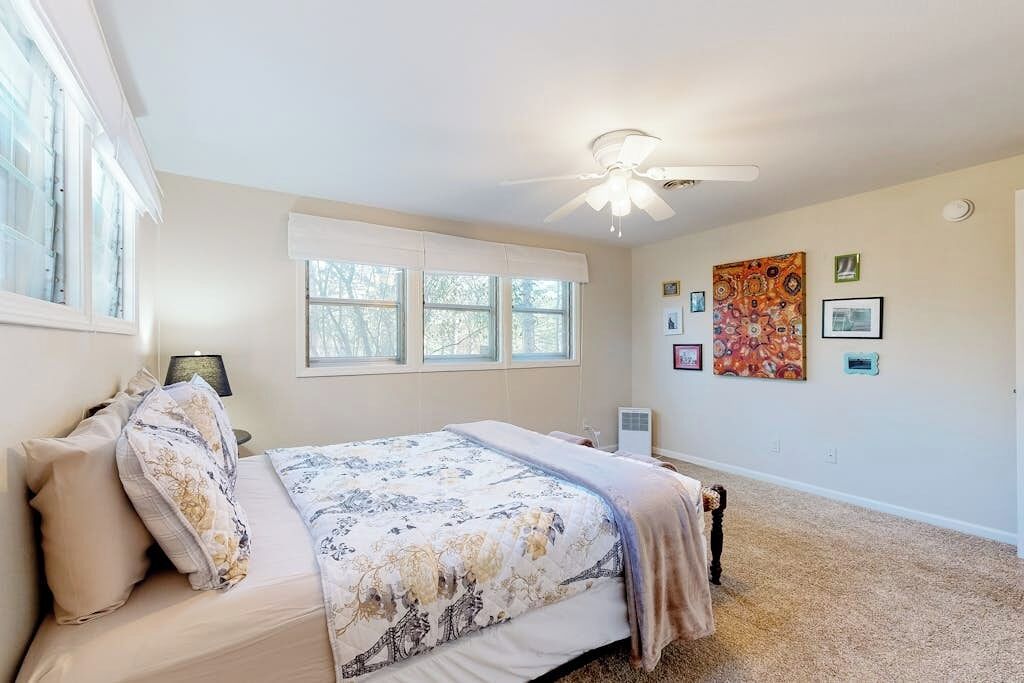 Une chambre à coucher avec un lit, un ventilateur de plafond, une fenêtre et des œuvres d’art murales.