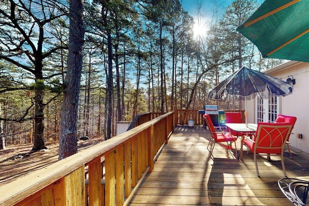 A wooden deck with a railing, surrounded by trees, and a patio area with outdoor furniture.