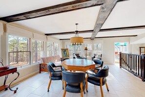 A spacious room with a large round table surrounded by chairs, a piano, and a view of trees through large windows. - Spacious 5BR - Fireplace - Deck - Firepit (Eureka Springs)