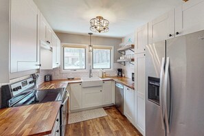 Eine moderne Küche mit weißen Schränken, einem Edelstahlkühlschrank und einer Holz Arbeitsplatte.