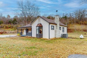 A single-story house with a stone chimney, a porch, and a small attached garage. - Whispering Trails | Bike-In/Bike-Out Retreat (Bentonville)