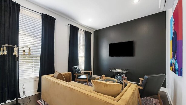 A modern living room with a sofa, chairs, a coffee table, and a flat-screen TV mounted on the wall. - Stylish 2BR -  W&D - Downtown Location (Bentonville)