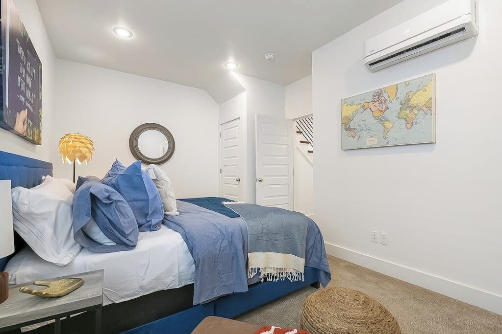 A bedroom with a bed, a map on the wall, an air conditioner, and a staircase.