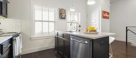 Una cocina moderna con una isla central, electrodomésticos de acero inoxidable y encimera blanca.